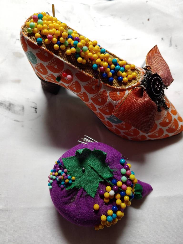 A shoe-shaped pin cushion next to the standard tomato pin cushion