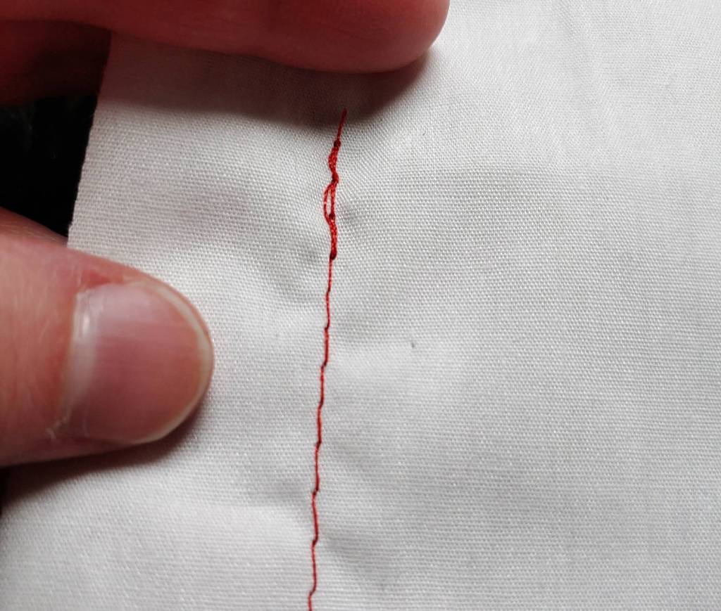 A straight red stitch on white fabric