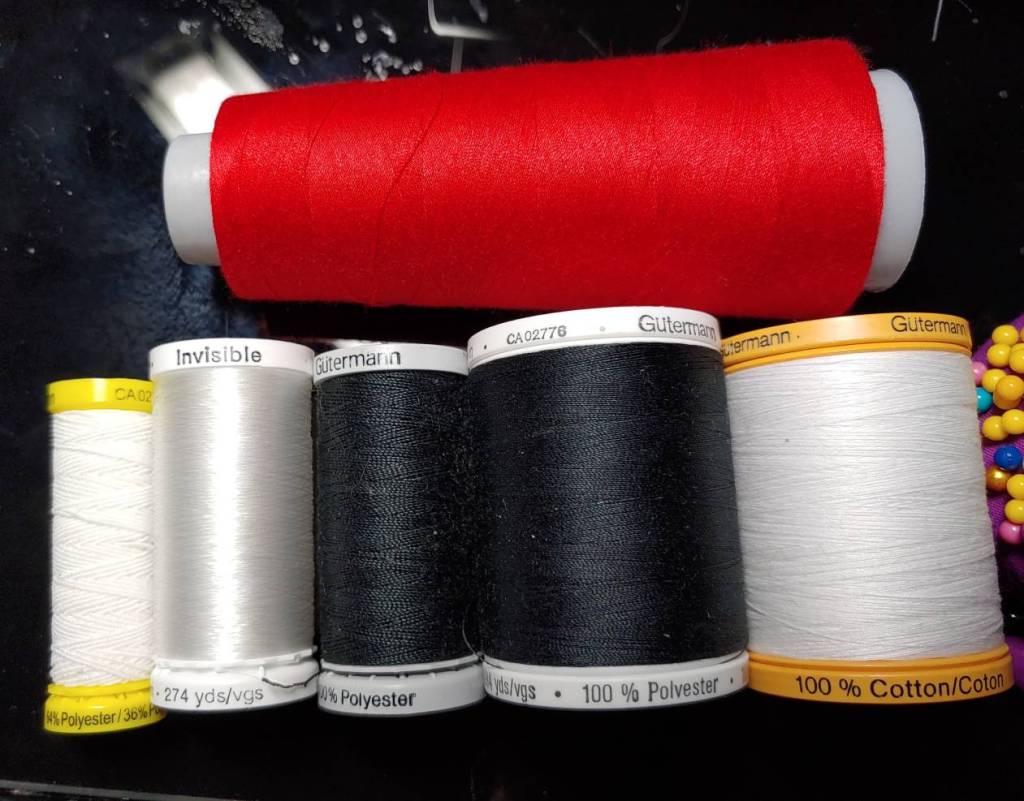 Several types of thread. Top: serger thread. Bottom (left to right): elastic, invisible, heavy duty, sew-all, and cotton