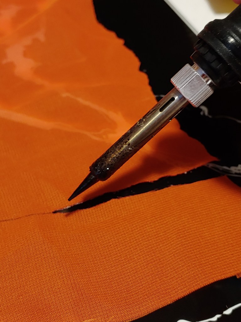 Making the first cuts in the fabric using the soldering iron like a pen and tracing the lines you've drawn.