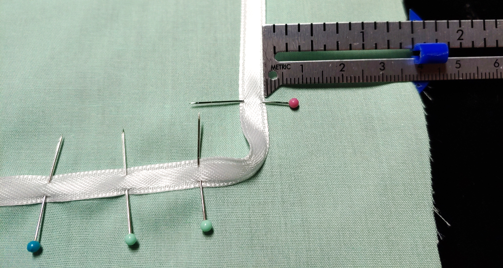 Sewing gauge shows the ribbon at 1½" from the edge, a pin keeping the ribbon in place as you work with the corner.