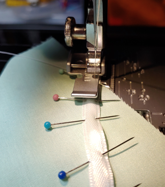 Sewing along the right edge of the ribbon, using the side of the zipper foot as a guide