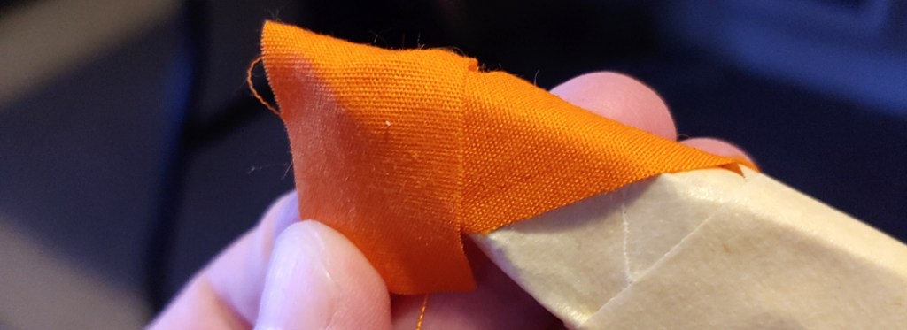 Piece of orange fabric wrapped around the point. The tails of the fabric are further wraped down around the shape.