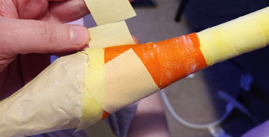 Adding decoupaged fabric strips around a shape covered in masking tape.