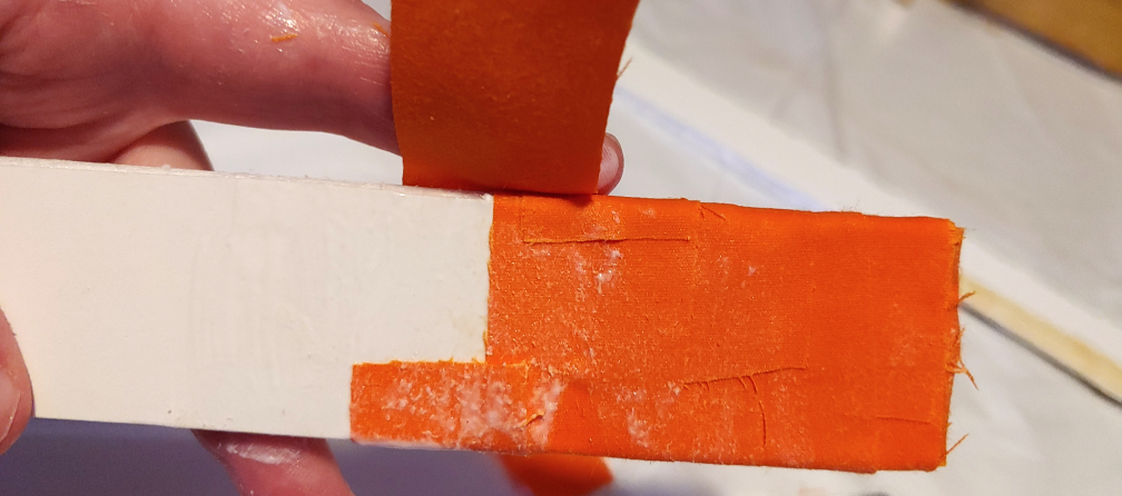 Wrapping an orange strip of fabric around a sword handle, on side at a time