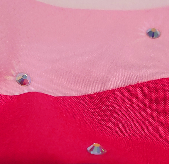 Several faceted rhinestones on bright pink fabric. they're casting light out on the surrounding fabric in beams