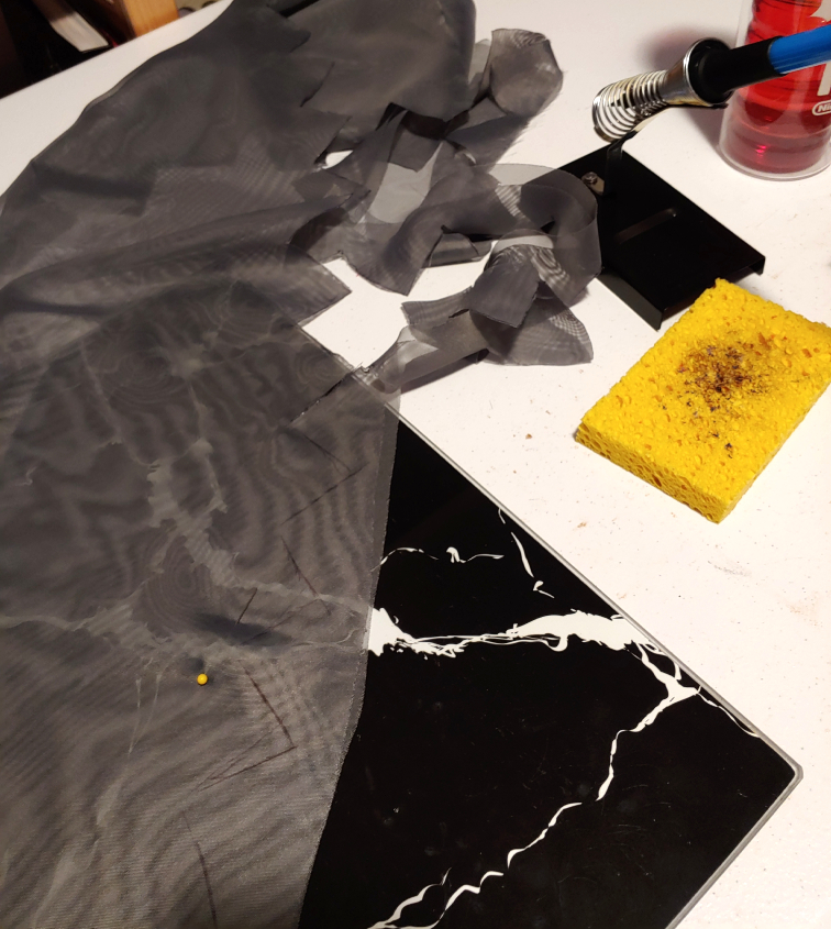 dark gray fabric laid over a black cutting board. zigzags are partially cut out using a soldering iron.