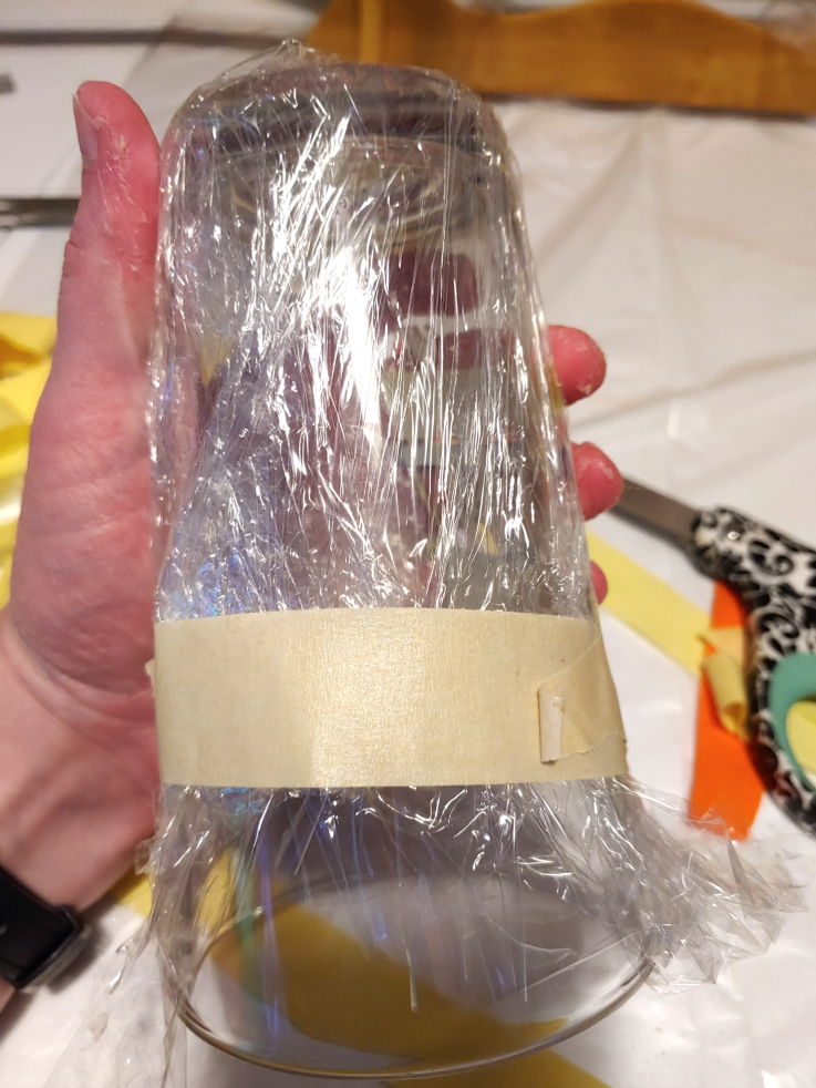 Covering the glass with plastic wrap. The wrap is then secured with a band of masking tape