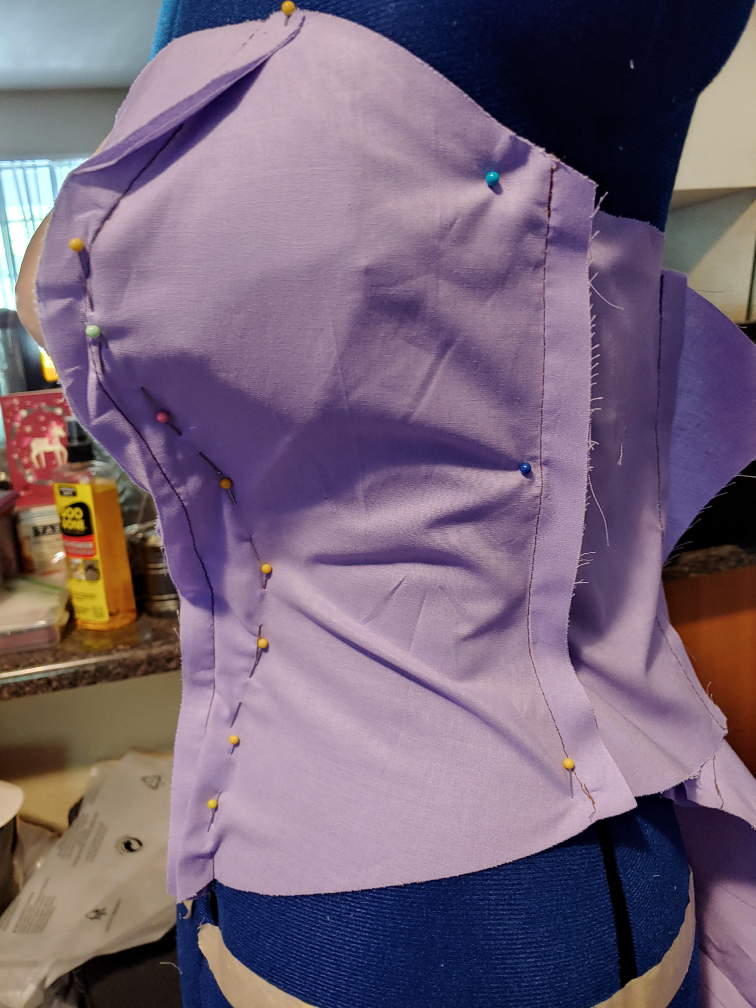purple corset fabric pinned to a dress form. Pins tighten the fabric along the bustline and curve in to meet the torso