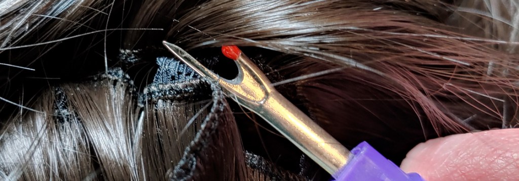 Ripping the threads behind the wefts removes them from the wig but keeps the wefts intact. The seam ripper is behind the weft and underneath a supporting thread in the wig itself.