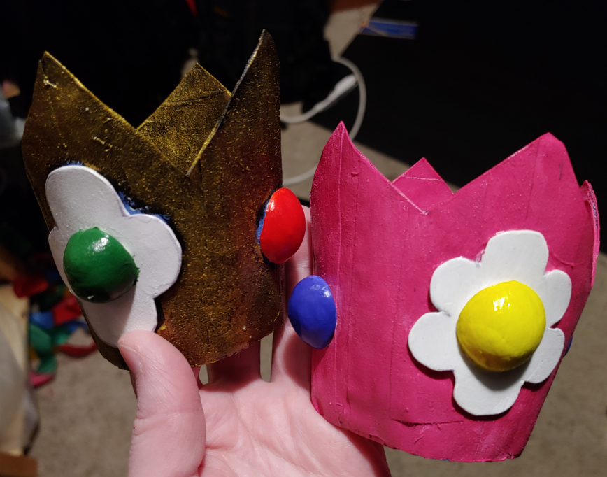 A pair of Princess Daisy crowns. Left, the current golden design. Right, the classic magenta design