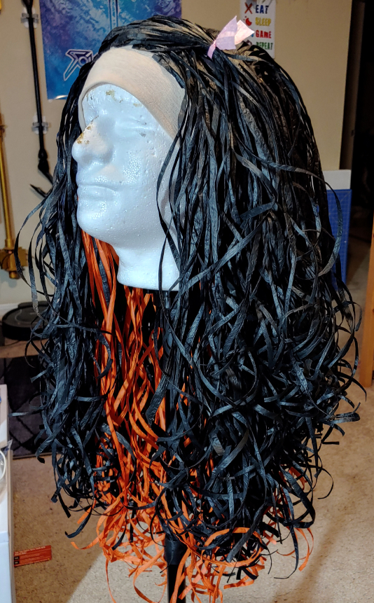 Finished paper raffia ribbon wig for Nezuko from Demon Slayer. Black raffia with a bright orange underlayer and a little pink bow in the bangs