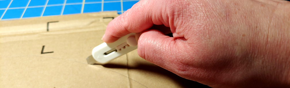 Scoring the cardboard with a box cutter. The box cutter is pushed only slightly into the cardboard to make the first scoring marks.