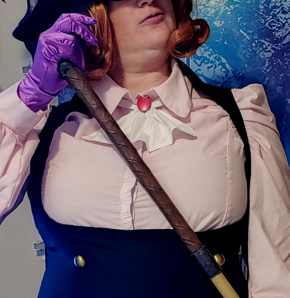 Finished axe handle held at a diagonal. A purple gloved hand holds the angled end cap.