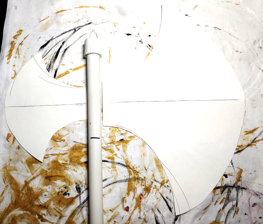 Axe head pattern made from poster board. The right axe head is much larger than the left. Both axe head pieces have been folded in half to make a mirrored pattern