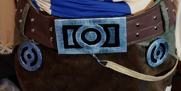 Finished belt buckle and accessories. Belt is brown pleather with silver studs threaded into green beltloops, decorated with dangling accessories