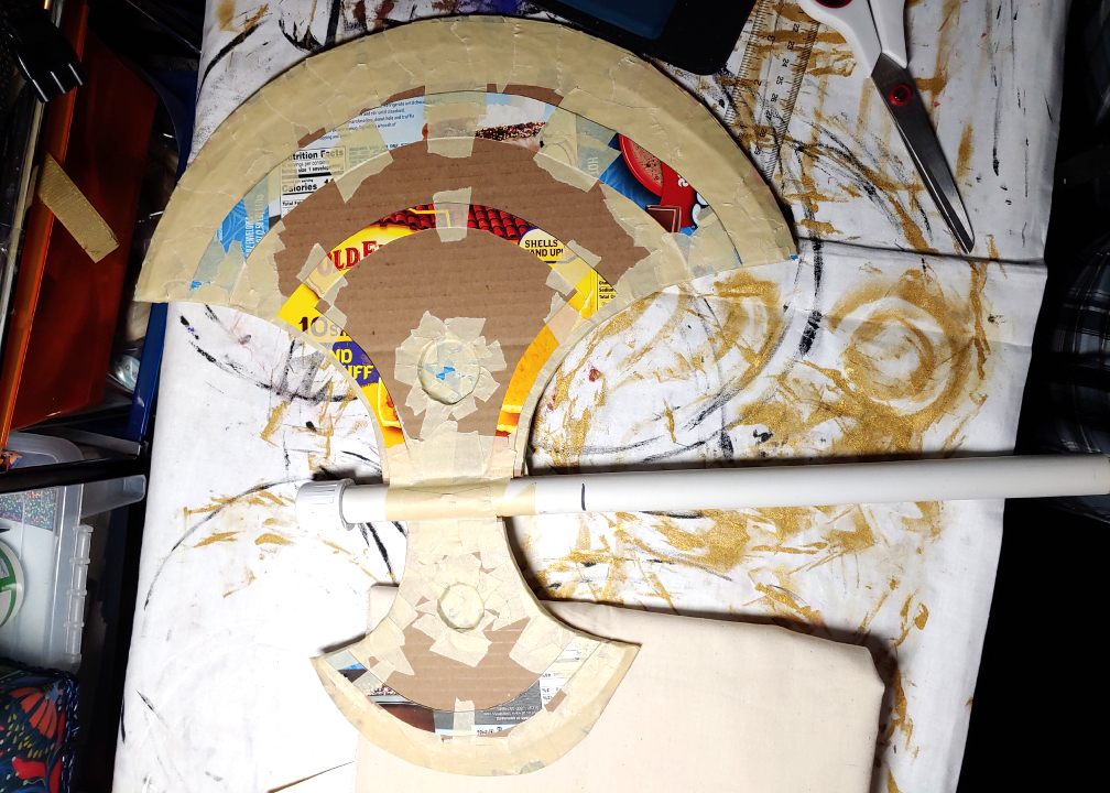 Using a PVC pipe to support an axe. Cardboard axe heads are taped to either side of the pipe using masking tape.