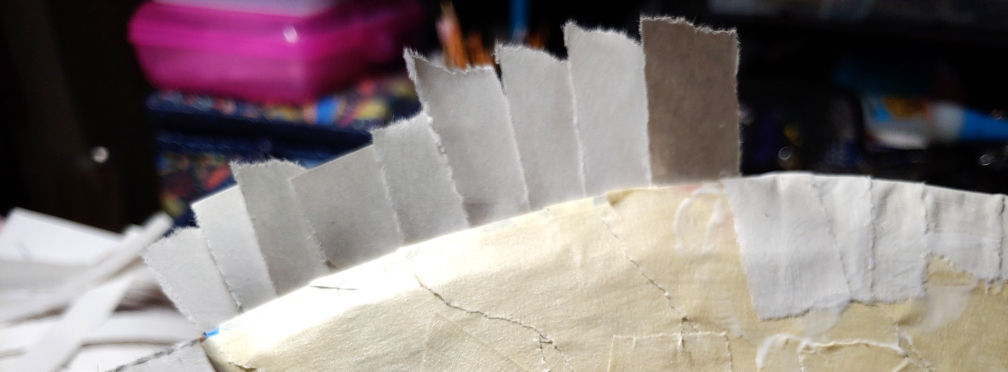 Wrapping the strips over an axe blade. The strips have been glued to the back already with half of them sticking up and half wrapped down on the front-facing side. Wrap the strips down and glue them like on the right to secure them over the edge