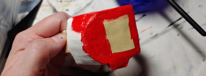 Painting the body color. Red is partially covering the white base coat and slightly overlapping the masking tape.