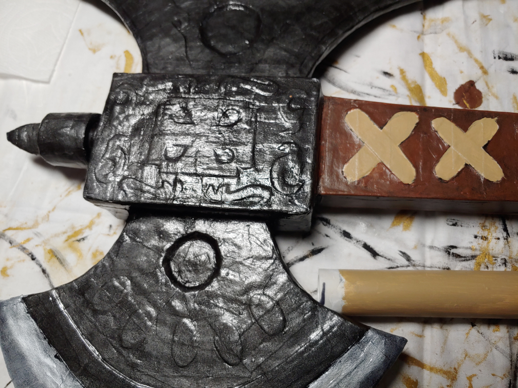 A dark silver axe with raised squiggles, lines, boxes , and laces.