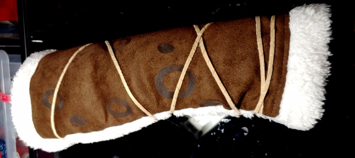 Suede arm guard painted with dark brown monster cheetah spots. The arm guard has a white fur edging with beige cording wrapped around it.