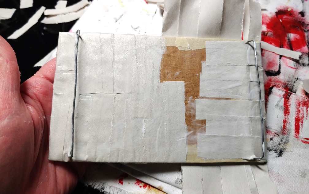 Wrapping the strips around the back of the buckle. The left side has been fully wrapped, while the right side only has the side wrapped and the top/bottom are still hanging over the edge