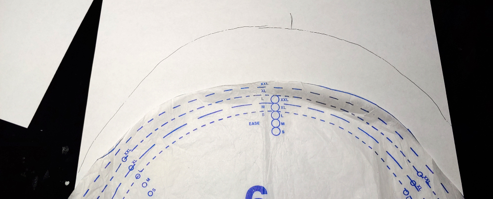 the sleeve pattern is traced onto some printer paper, a line marking the shoulder seam is protruding off the top of the curve