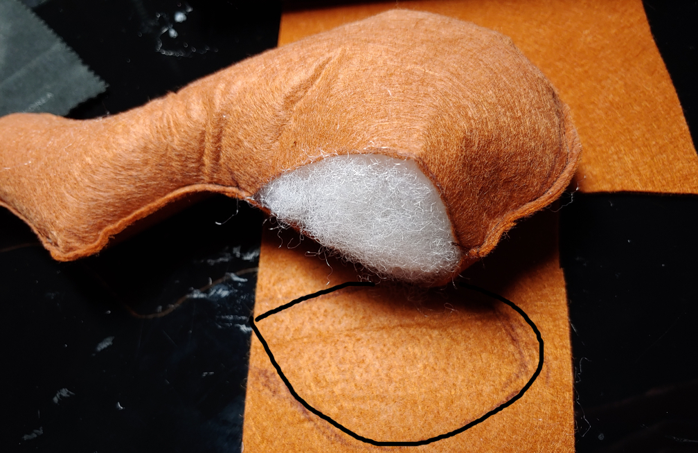 Stuffed pillow with cap traced on felt. The pillow is on the top with white fiberfill showing in the opening. The cap is traced in a teardrop-like shape (outlined in black)