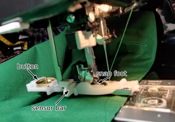 The buttonhole foot attached to the sewing machine. The text from left to right reads:
- button
- sensor bar
- snap foot