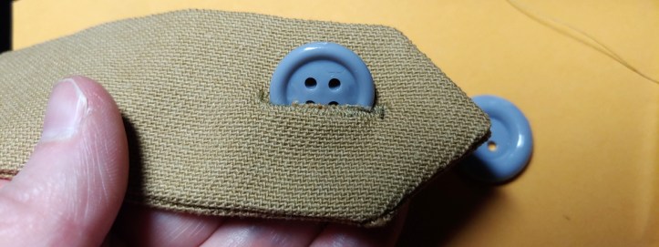 Inserting the button. A gray button is sticking half out of a buttonhole. Hey look, it works!