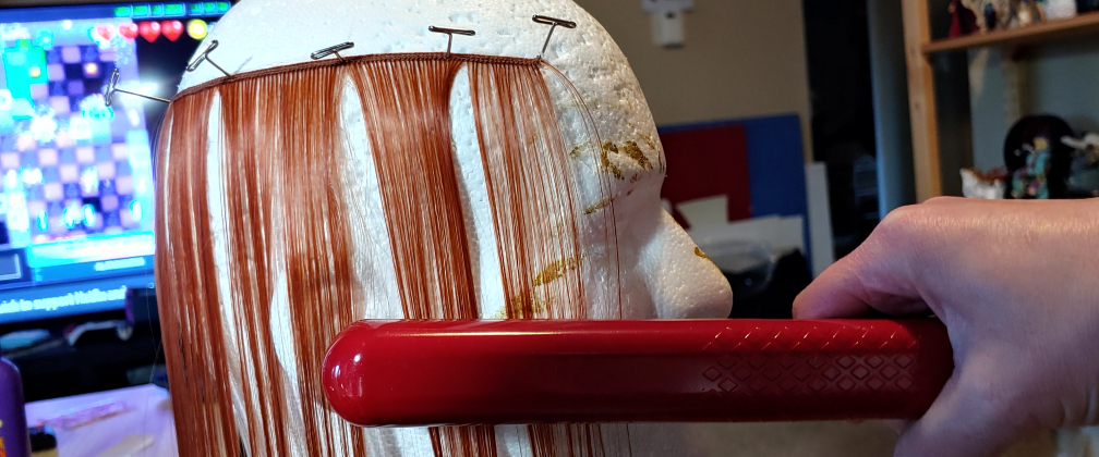Heating up the fibers with a flat iron. Wefts are pinned to a wig head using T-Pins and heated up with a red flat iron