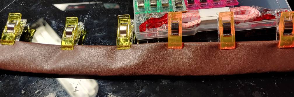 Yellow and orange fabric clips on the edge of a brown tablecloth belt with a box of clips in the back.