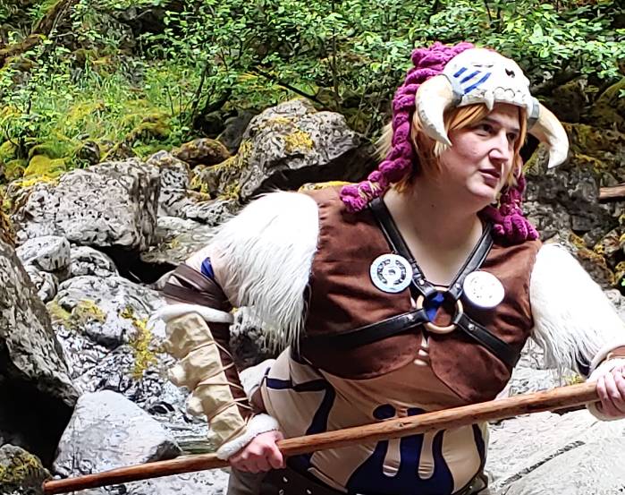 Arm bone on the finished cosplay posing with a wooden staff in the middle of the forest