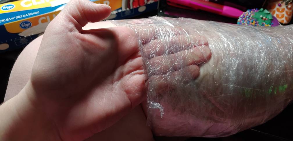 Checking to make sure there's enough space at the calf to get scissors underneath. Four of my fingers are tucked underneath the cling wrap and tape.