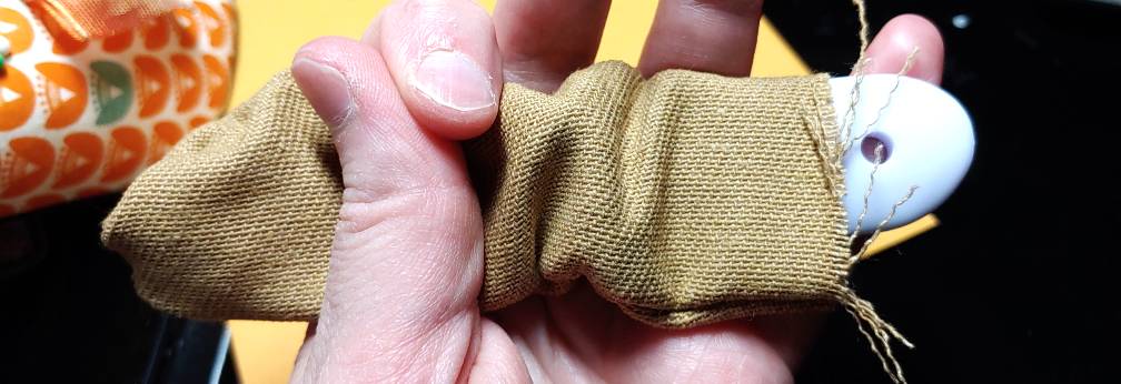 Turning the tab right-side out with a point turner. The white point turner peeks out from the beige fabric on the right side underneath the raw, fraying edge.