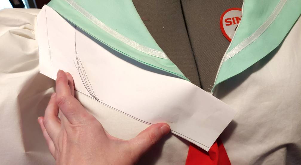 Patterning the scarf tie. The red tie is pinned to the front center of the shirt with a folded piece of printer paper held up underneath the green collar.