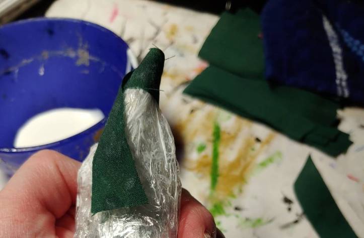 Starting the decoupage process by wrapping the tip with fabric. Green fabric wraps around the plastic wrap now slathered in white glue.