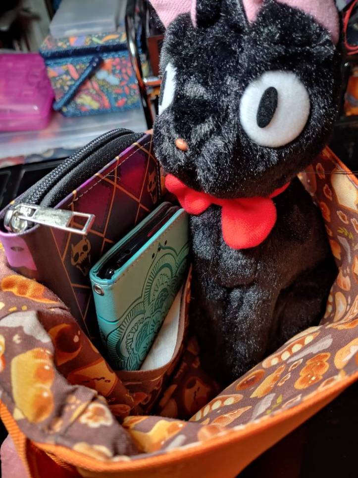 Jiji plush sitting inside the bag with a phone and wallet with more room to spare