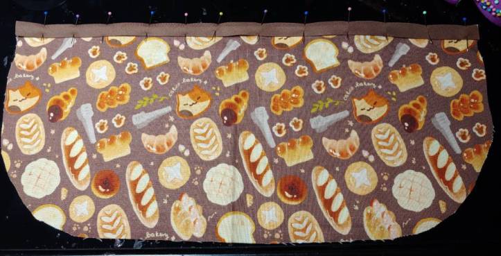 Brown bias tape pinned to the top of the pocket. Sew along the bottom edge here