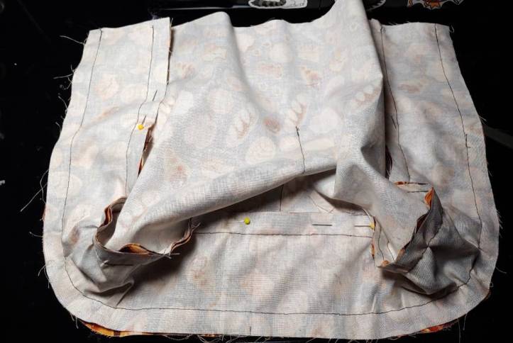 Gusset fully sewn and pinned out of the way to make it easier to see when sewing. Pins are along the top of the gusset, partially hidden in the folds of the body piece on top.