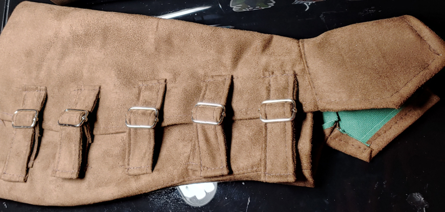 Suede leg guard with multiple slider buckle closures. Leg guard is pictured sideways with the foot guard on the right side.