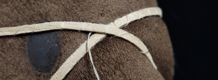 Sewing beige suede cord onto brown suede using a whip stitch to make a wrapped look