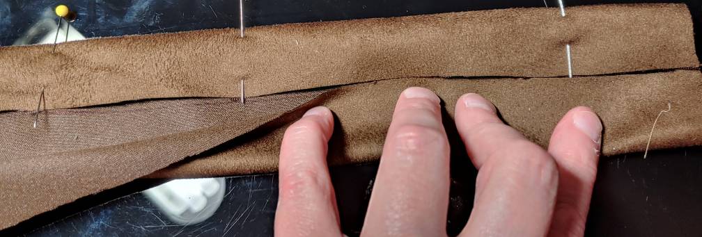 Folding suede into a strip for buckles. The right side of microsuede has a fuzzy look while the wrong side has a coarser, woven look. The strip is folded open on the left to show the rough inside of microsuede