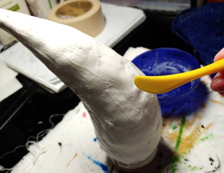 Flat yellow clay knife used for carving. The clay horn is still wet from a good slathering right before this. A blue bowl of water sits in the background.