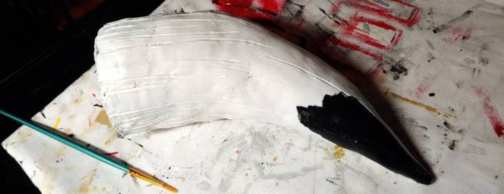 White drinking horn with a partially painted black coat along the tip. A green paintbrush sits off to the left side.