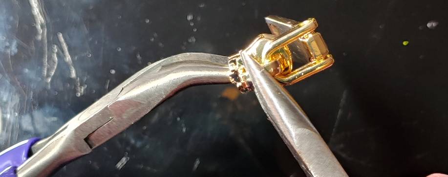 Pulling the slider apart with a curved and flat pair of pliers. The curved pair is on the left with the flat on the right.