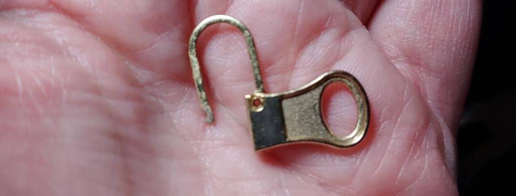 A hinged pull tab replacement from a zipper repair kit with the hinge opened