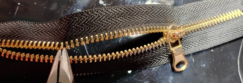 Pulling the first tooth at the top of the zipper. The teeth are bending around the pliers to make room for them.