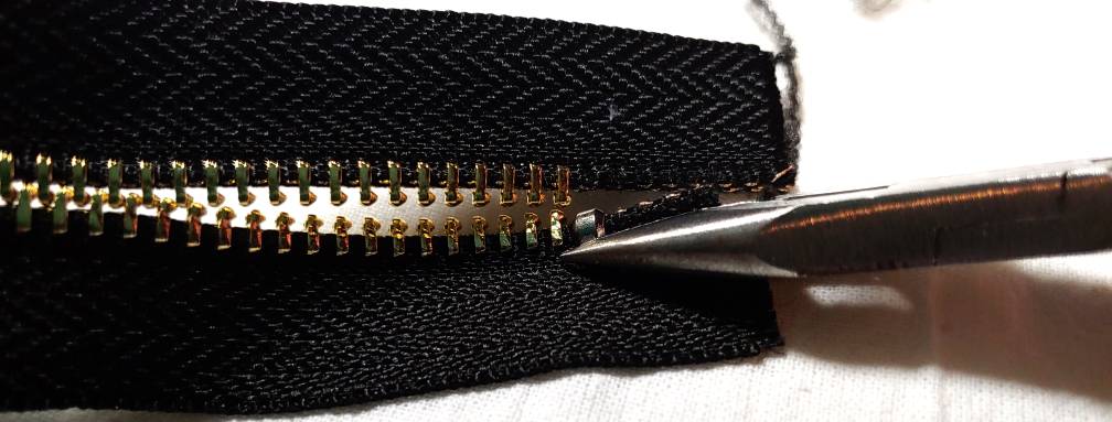 Adding one top stop with a pair of pliers. The pliers are on the right with a small silver stop sitting in near the edge of the needle-nose.