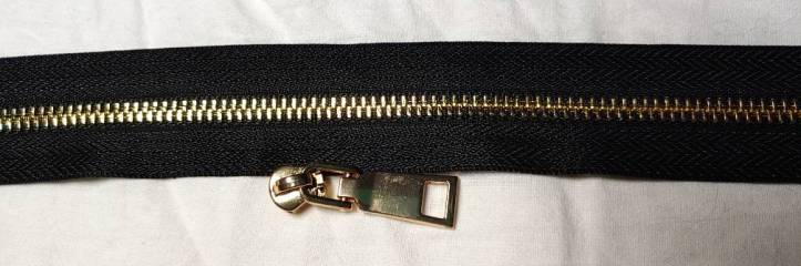 gold metal zipper with black tape and a gold zipper pull sitting below it